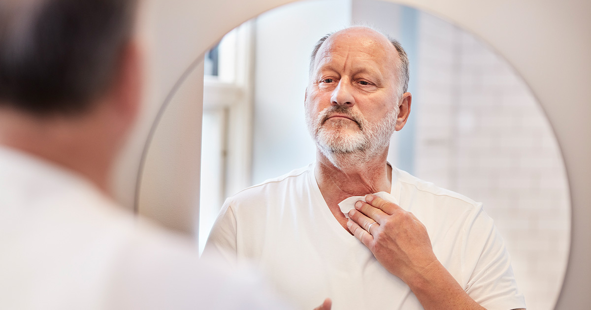 man cleaning his neck stoma in front of mirror