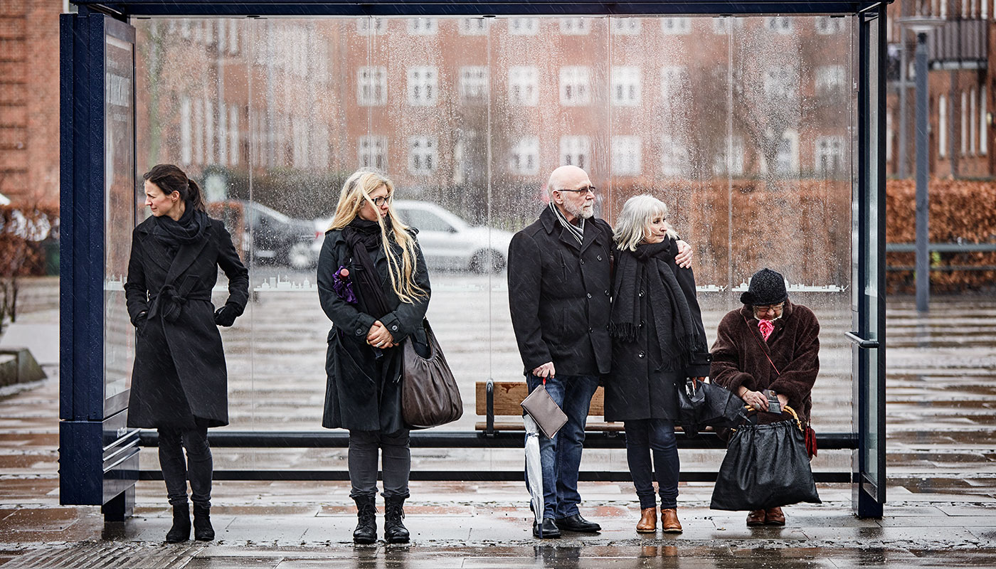 Man with a neck stoma waiting in the bus stop while using a Provox Life HME.