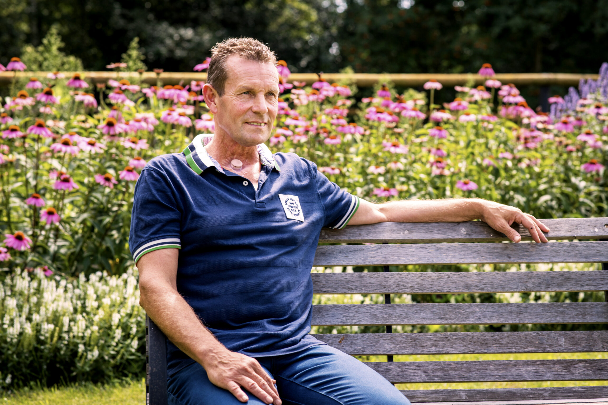 Man with laryngectomy stoma sitting outside in garden with flowers HME