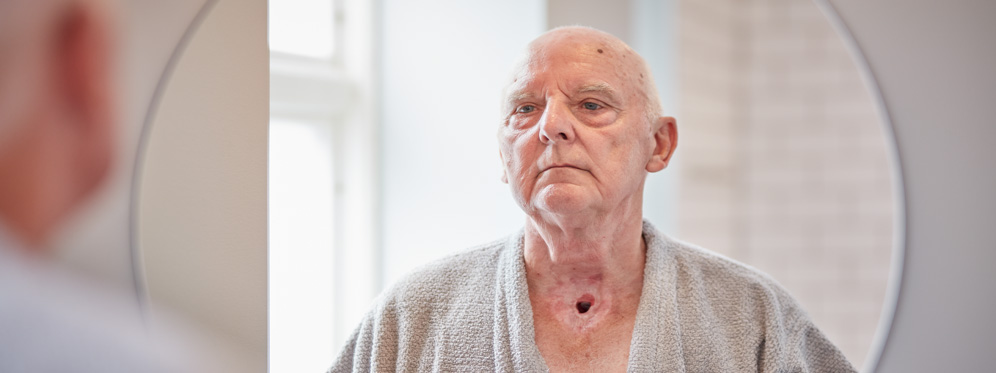 man with a neck stoma standing in front of mirror